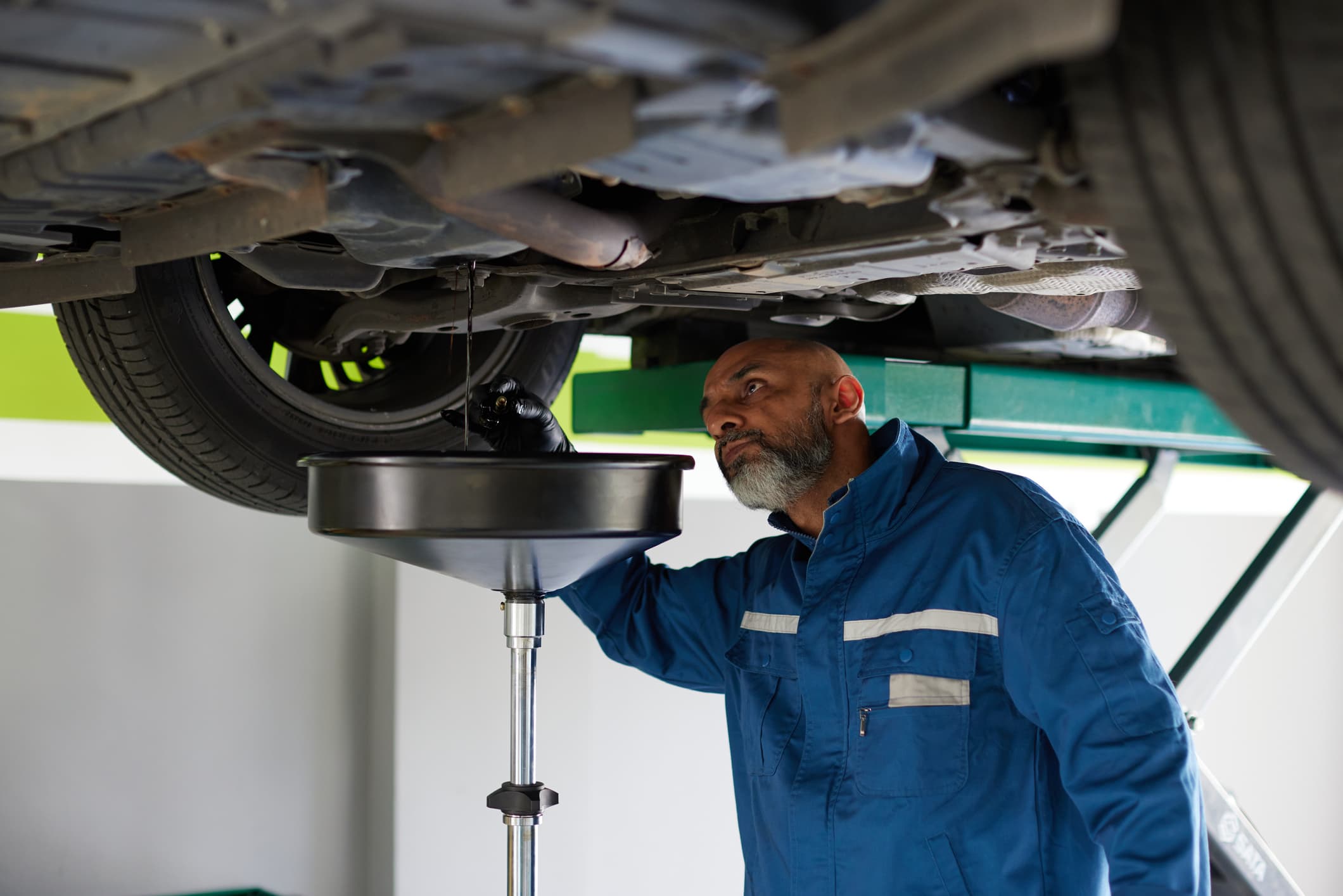 Asian car mechanic performs oil change for customer in car workshop